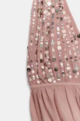 Top halter de color rosado con escote en pico pronunciado, confeccionado en tejido semitransparente con efecto arrugado y detalle de lentejuelas brillantes en la parte superior. Cuenta con tirantes para anudar al cuello y espalda descubierta con lazo ajustable.