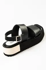 Sandalias negras de cuero con plataforma blanca y hebilla metálica.