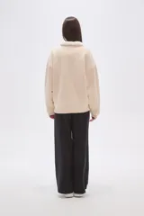 Buzo de algodón color tostado, con cuello polo y cierre frontal parcial con botones. Presenta un detalle de forro de corderito sintético blanco en el cuello y mangas largas con diseño holgado.