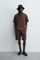 Bermuda de corte relajado color marrón oscuro, confeccionada en tejido jacquard con textura acanalada vertical. Presenta cintura elástica ajustable con cordón, bolsillos delanteros y un bolsillo trasero de plastrón.