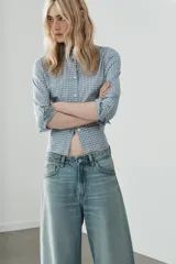Jeans de tiro medio con cinco bolsillos, trabillas y cierre frontal con cremallera y botón metálico. Presenta un diseño baggy con piernas anchas, roturas decorativas y dobladillo vuelto en los bajos.
