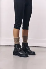 Botinetas de cuero negro con suela track, punta cuadrada y doble hebilla metálica decorativa en el lateral. Diseño de caña corta con cierre lateral.