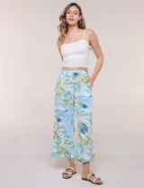 Pantalón crop de lino y rayón, con diseño wide leg de corte holgado, estampado tropical de hojas en tonos verde, azul y marrón sobre fondo blanco. Cuenta con pretina trasera elastizada y bolsillos delanteros.