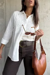 Camisa blanca de manga larga con cuello clásico y cierre frontal de botones. Presenta un diseño con paneles de encaje bordado en la parte superior delantera, confeccionada en tejido con textura.