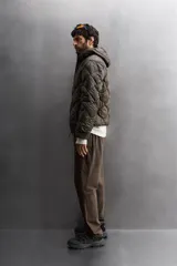 Campera puffer verde oliva acolchada con diseño de rombos, capucha y cierre frontal con cremallera. Incluye bolsillos laterales con cierre. Relleno de plumón y plumas.