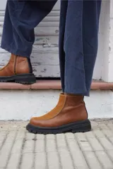 Bota corta de cuero color marrón con paneles en gamuza al tono, diseño de punta redondeada y suela track negra de goma. Presenta cierre lateral y detalle de costuras a la vista.