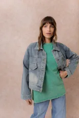 Campera de denim con lavado claro y efecto desgastado. Presenta cuello camisero, cierre frontal con botones metálicos, dos bolsillos frontales con tapa y botón, y puños abotonados.
