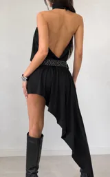 Vestido corto negro con escote halter y diseño asimétrico, con una caída más larga en la parte posterior. Presenta un corte holgado y fluido.