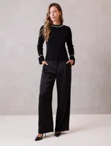 Buzo de tejido soft color negro, con cuello a la base y mangas largas. Presenta apliques de perlas decorativas en el contorno del cuello y en los puños.