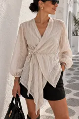 Camisa cruzada de color beige con diseño a rayas sutiles, escote en V cruzado, mangas largas abullonadas con puños ajustados y lazo ajustable en la cintura.