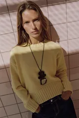 Sweater de punto color amarillo claro, con cuello redondo, manga larga y dobladillo asimétrico más largo en la parte trasera. Presenta acabados en rib en cuello, puños y ruedo.