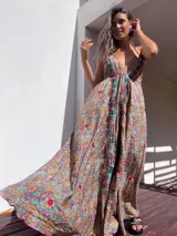 Vestido largo de estilo boho, con estampado tipo paisley en tonos tierra, turquesa y rosa. Presenta un escote profundo con tirantes finos y detalles de bordados florales en color rojo y verde a lo largo del frente.