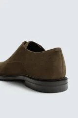 Zapato tipo derby con cordones, confeccionado en piel con acabado de serraje. Presenta horma redonda y suela a contraste.