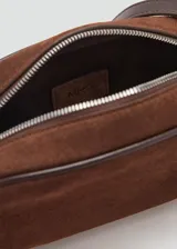 Bolso bandolera de tamaño pequeño confeccionado en piel de serraje color marrón. Cuenta con cierre de cremallera, forro interior de algodón y asa larga ajustable con hebilla metálica.