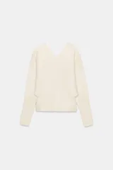 Jersey liso color blanco hueso, con cuello pico, manga larga y sisa ancha que se estrecha hacia la muñeca.