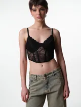 Corset de encaje negro con diseño estructurado, copa preformada con aro y ballenas frontales. Presenta breteles elásticos ajustables y cierre posterior con broches.