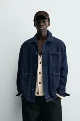 Chaqueta de denim de algodón en color azul oscuro con corte relaxed fit. Presenta cuello de solapa, cierre frontal con botones metálicos y tres bolsillos de parche en el delantero. Las mangas son largas con puños abotonados.