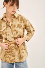 Campera de corte recto confeccionada en gabardina de algodón, con diseño estampado y detalles bordados. Presenta cuello camisero, cierre frontal con botones, bolsillos con solapa en el pecho y lazo ajustable en la cintura con terminaciones bordadas.