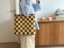 Bolso tipo tote de cuero trenzado a mano con diseño de damero en colores marrón y beige. Cuenta con doble asa trenzada y forro interior.