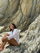 Camisa de lino color marrón rojizo, con cuello clásico y botones frontales blancos. Presenta pliegues verticales en el torso y mangas largas abullonadas con frunces elásticos en los puños.