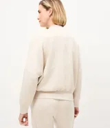 Campera bomber deportiva de mujer color beige, confeccionada en modal con cierre frontal por cremallera, cuello medio y bolsillos. Presenta mangas largas con puños elásticos y elástico en la cintura.