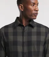 Camisa de hombre de manga larga, confeccionada en franela de algodón, con cuello inglés y abotonadura frontal. Presenta un estampado de cuadros grandes en tonos verde oliva y negro.