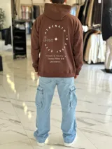 Canguro oversize marrón con capucha, bolsillo tipo canguro y diseño estampado en la espalda con el texto "Be Brave" y detalles tipográficos en color blanco.