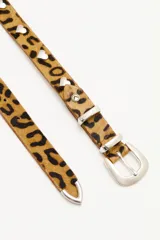 Cinturón de cuero vacuno con acabado de pelo animal print, de 2,5 cm de ancho. Presenta remaches metálicos en forma de corazón, hebilla, pasador y puntera metálica en tono plata.