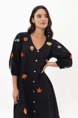 Vestido largo blanco de algodón con bordados de motivos marinos en tonos naranja, verde y azul. Tiene escote en V, mangas 3/4 abullonadas y cierre frontal con botones.