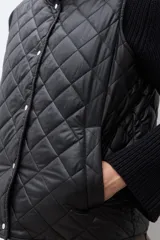 Chaleco capitoneado reversible con cuello alto, cierre frontal con botones a presión y bolsillos delanteros. Presenta un diseño bicolor en tonos verde oliva y beige con detalles en negro.