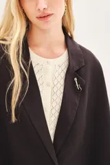 Saco de lino y liocel de corte amplio, con solapa, bolsillos falsos y mangas de largo regular. Incluye un pin decorativo en la solapa.
