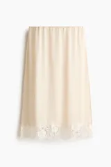 Pollera midi de corte holgado color beige, con elástico oculto en la cintura, detalle de encaje floral en el bajo y tajo lateral pronunciado.