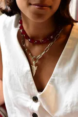 Collar doble de acero quirúrgico compuesto por una gargantilla de cuentas de piedra color rojo y una cadena de eslabones plateados con un dije central en forma de punta de flecha.