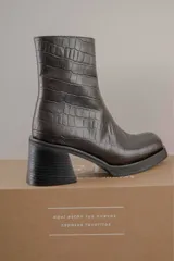 Bota de caña media con punta cuadrada, confeccionada en cuero gamuzado color marrón, con taco bloque y suela de goma negra.
