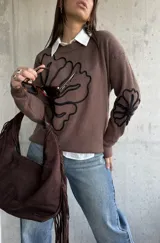 Sweater de punto color chocolate con diseño de flores bordadas en hilo negro en el frente y en una de las mangas. Presenta cuello redondo y puños acanalados.