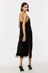 Vestido largo negro de jacquard, con tirantes finos ajustables, escote en V y falda evasé con aberturas laterales. Cuenta con apliques de encaje transparente en el busto, el centro y el bajo.