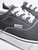 Championes de lona color azul grisáceo, estilo skate o casual, con cordones blancos y suela de goma blanca con una línea fina azul en el borde.