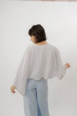 Blusa de lino color blanco, de diseño holgado, manga larga amplia acampanada con detalles de bordado en los puños y cuello redondo.