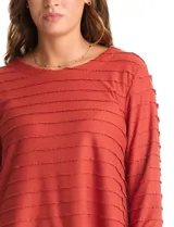 Blusa de tejido shaggy color terracota, con cuello a la base, mangas tres cuartos con tajo lateral en el puño y ruedo redondeado con largo posterior asimétrico.