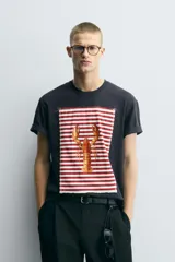 Camiseta azul marino de corte relaxed fit, cuello redondo y manga corta. Presenta un parche rectangular estampado con rayas horizontales rojas y blancas, y un dibujo de una langosta en el centro.