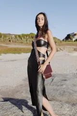 Vestido midi de cuero negro con diseño cut-out en la cintura, escote strapless y tajo lateral en la falda.