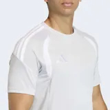 Remera deportiva Adidas Tiro26 League, color gris claro, de manga corta y cuello redondo. Presenta paneles blancos en los hombros y tres franjas blancas en los hombros. Incluye logo Adidas en el pecho.