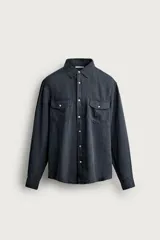 Camisa relaxed fit de lino color negro con efecto lavado, cuello clásico, manga larga con puños abotonados y dos bolsillos de parche con solapa en el pecho.