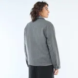 Sobrecamisa de corte recto y diseño estructurado, confeccionada en tejido gris con patrón de rayas verticales finas. Presenta cuello clásico, cierre frontal con botones y dos bolsillos frontales con solapa.