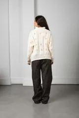 Cárdigan de punto color blanco con diseño calado de motivos florales, cuello alto, cierre frontal con botones y mangas largas con puños acanalados.
