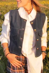 Chaleco de denim azul oscuro, con corte entallado, cierre frontal con botones dorados y bolsillos delanteros con solapa.