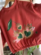 Buzo cropped de algodón color rojo con estampa frontal exclusiva de corazones con diseño de cerezas y hojas, manga larga y cintura elastizada.