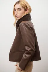 Chaqueta corta color beige con cuello de piel sintética negra, cierre frontal de botones y bolsillos laterales.