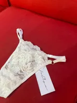 Tanga de encaje blanco con tiras laterales regulables y argollas doradas.