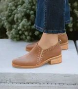 Zapato de cuero vacuno color tostado, con diseño de botineta baja, taco cuadrado de madera y detalle de perforaciones decorativas en el empeine.